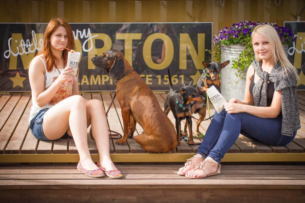 Kaksi hymyilevää tyttöä ja ruskea koira istuskelevat Varkauden Mortonin portailla.